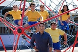 A man in a blue shirt poses for a photo with five primary school kids perched in a climbing apparatus