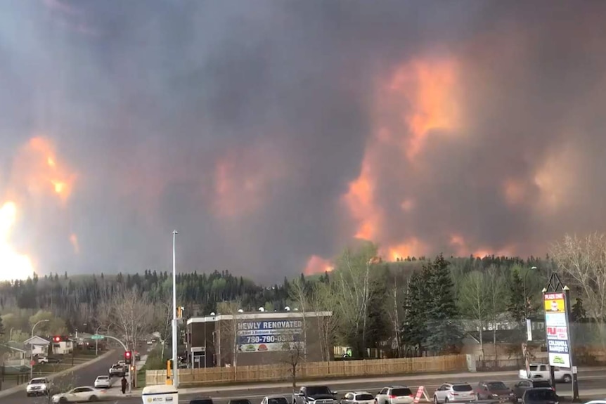 Fire and smoke fills hills behind cars and shops in Fort McMurray