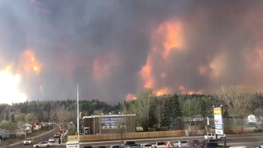 Fire and smoke fills hills behind cars and shops in Fort McMurray
