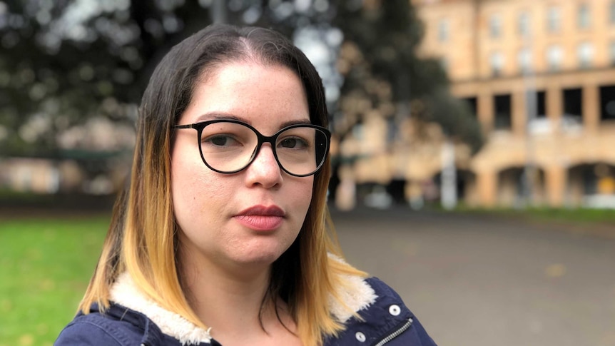 Renata Tavares Silva sitting on a park bench, she is wearing glasses and looking at the camera.