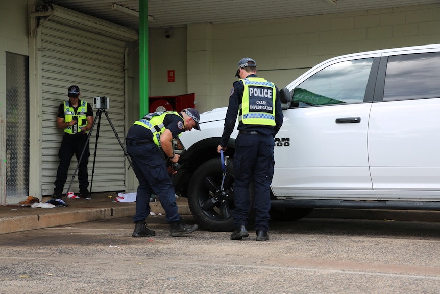 Several police officers inspect the wheel of a ute in a shopping centre carpark.