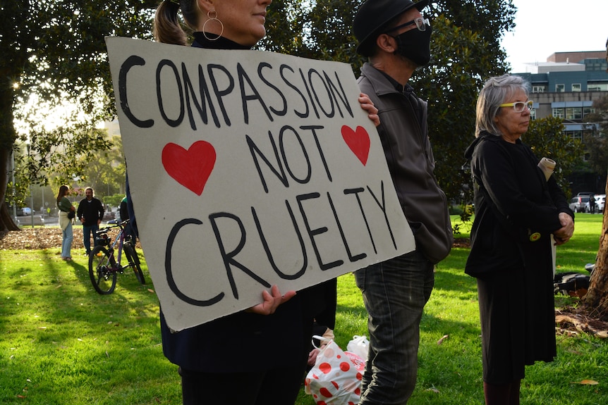 A woman holds a sign reading: 'Compassion not cruelty' with red love hearts.