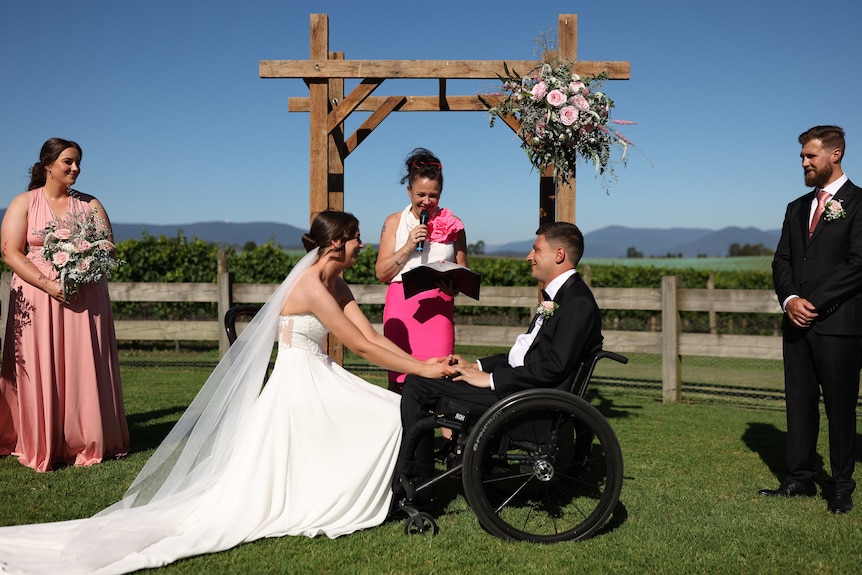 A couple gets married, with the groom in a wheelchair.
