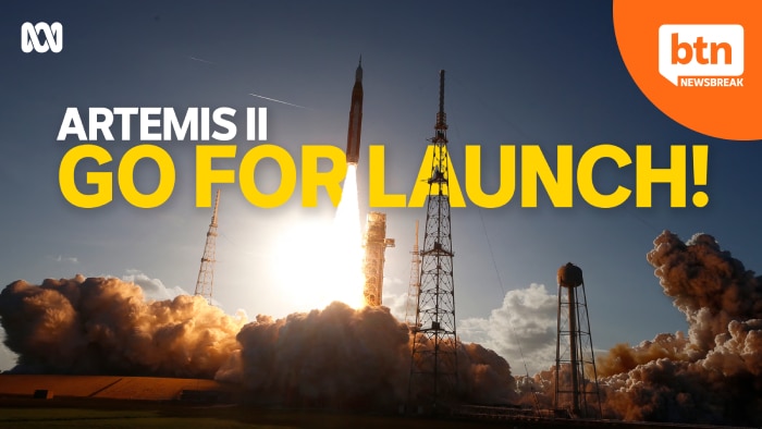 Rocket launch with bright flames and smoke, under a blue sky. Text: ARTEMIS II GO FOR LAUNCH!