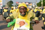 A man rides a motorcycle dressed in yellow with a picture of Ugandan President Yoweri Kaguta Museveni on the front.