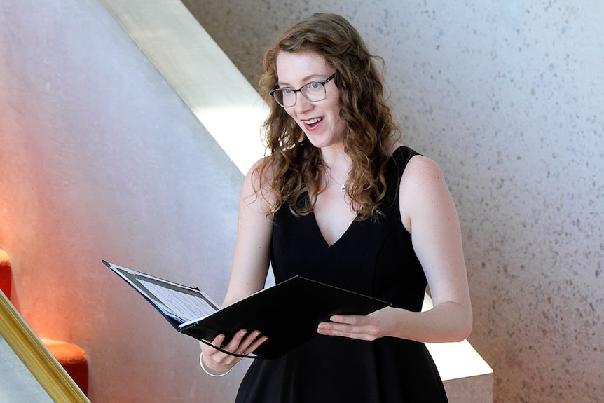 Soprano Veronica Milroy performing while holding a music sheet book.