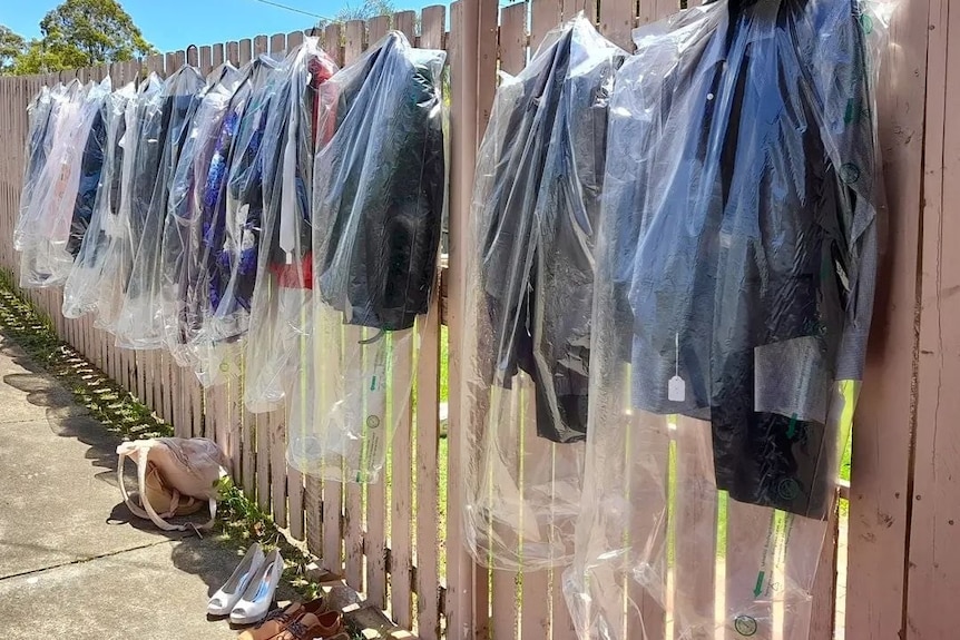 Donated formal suits hang on a fence with shoes.