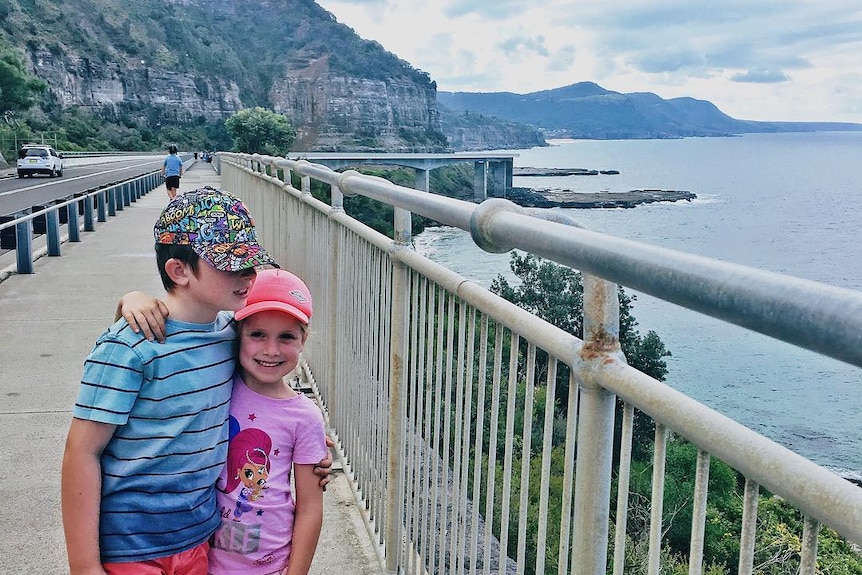 A little sister hugs her big brother overlooking the ocean