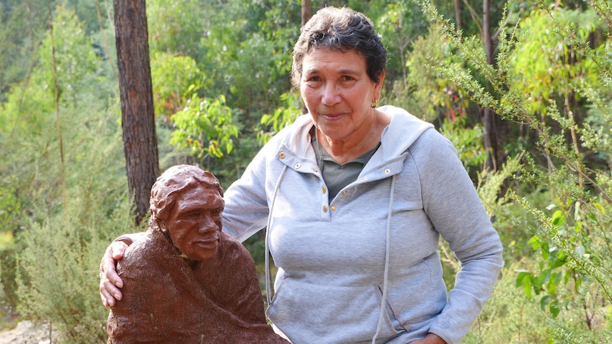 An Aboriginal woman with her arms around a statue of a woman. 