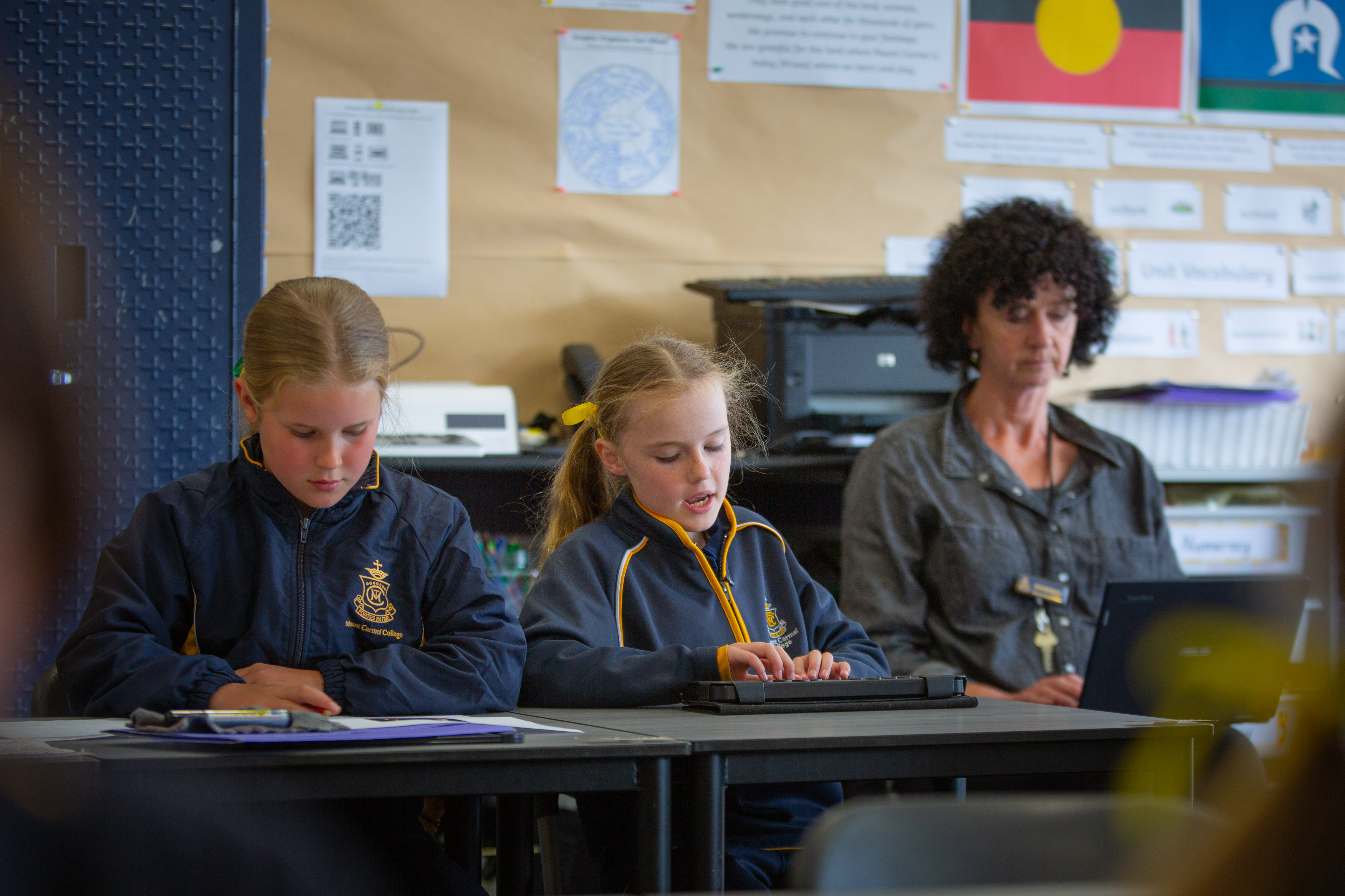 Una niña con lazos amarillos en el pelo sentada en un escritorio en un salón de clases leyendo en un dispositivo Brailliant.