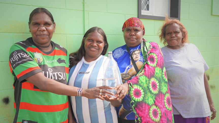 Four women stand together with a bottle of water