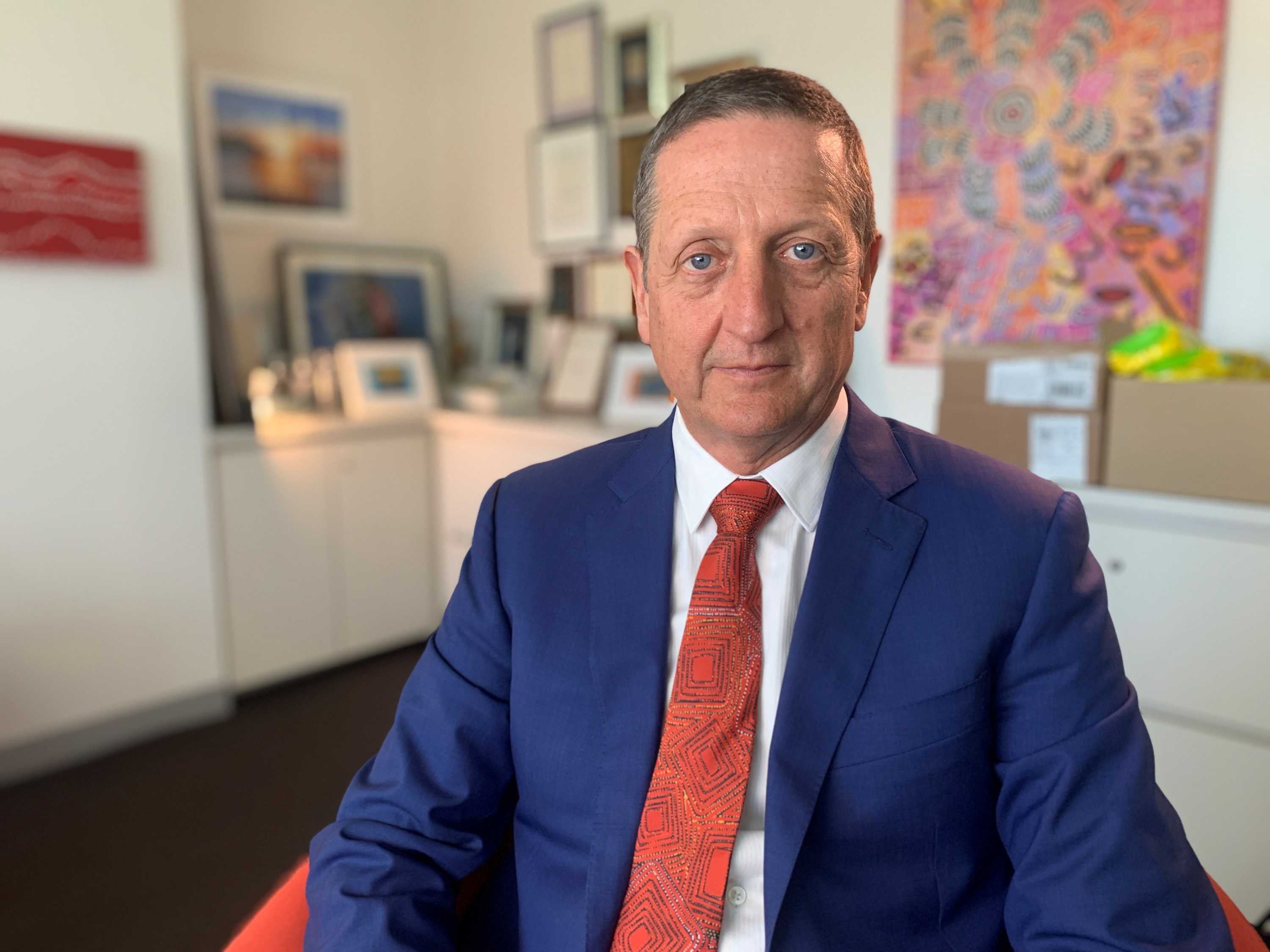 Professor Ian Hickie wears a blue suit and red tie and looks into the camera from an office space.