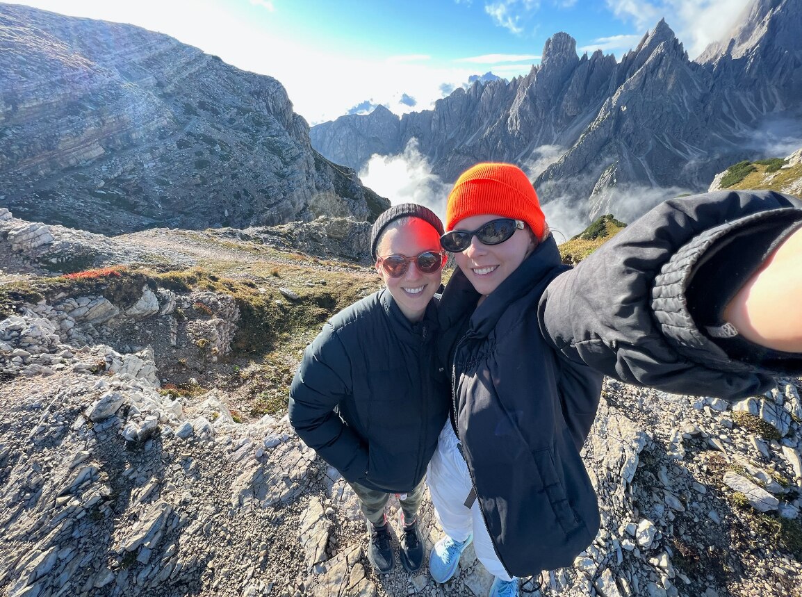 A couple rugged up in jackets take a selfie atop a rocky Italian mountains while on holiday.