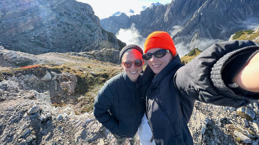 A couple rugged up in jackets take a selfie atop a rocky Italian mountains while on holiday.