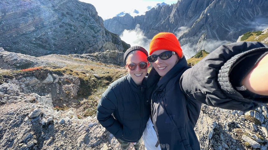 A couple rugged up in jackets take a selfie atop a rocky Italian mountains while on holiday.