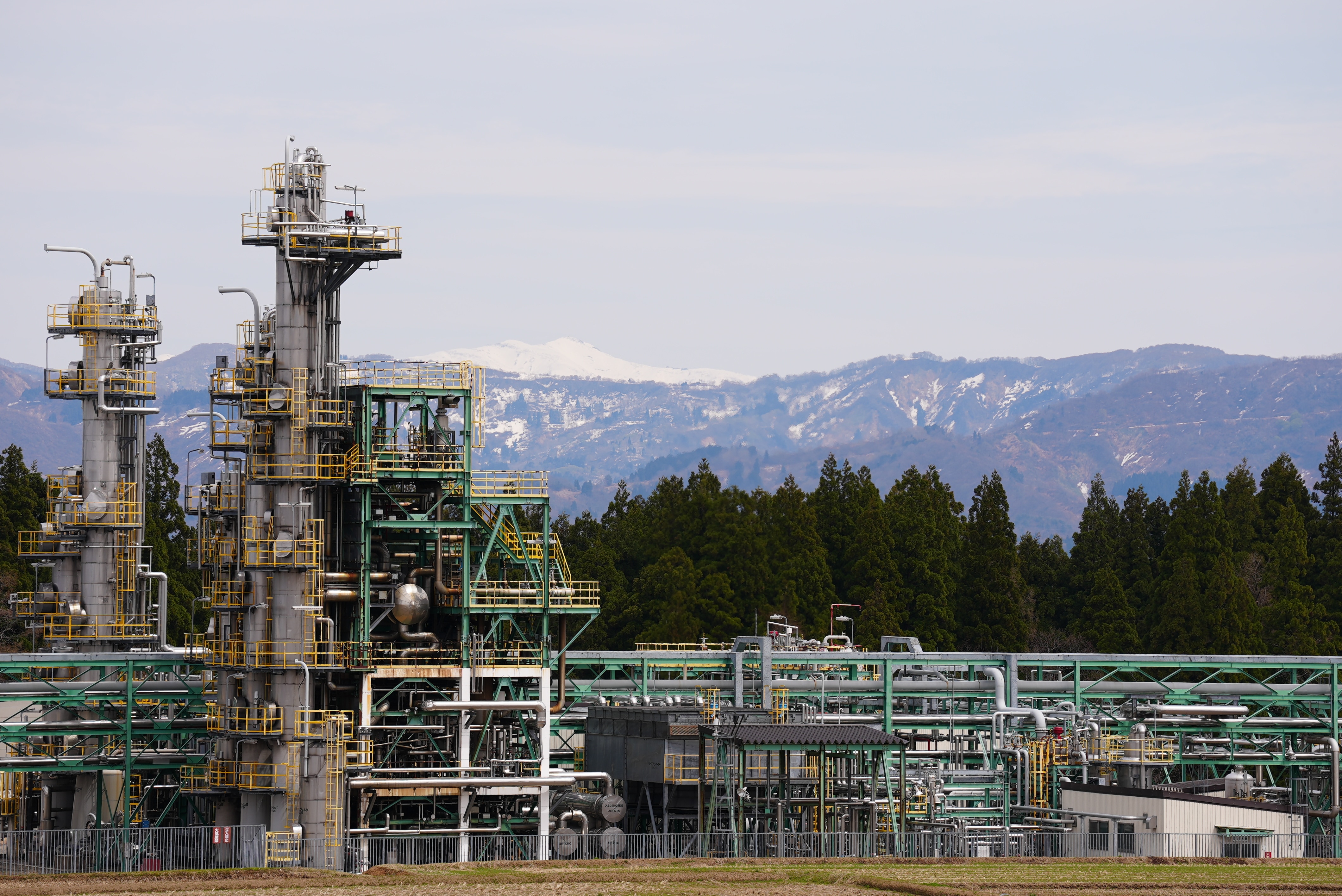 Two oil towers surrounded by pipes overlooking Japan's mountain.