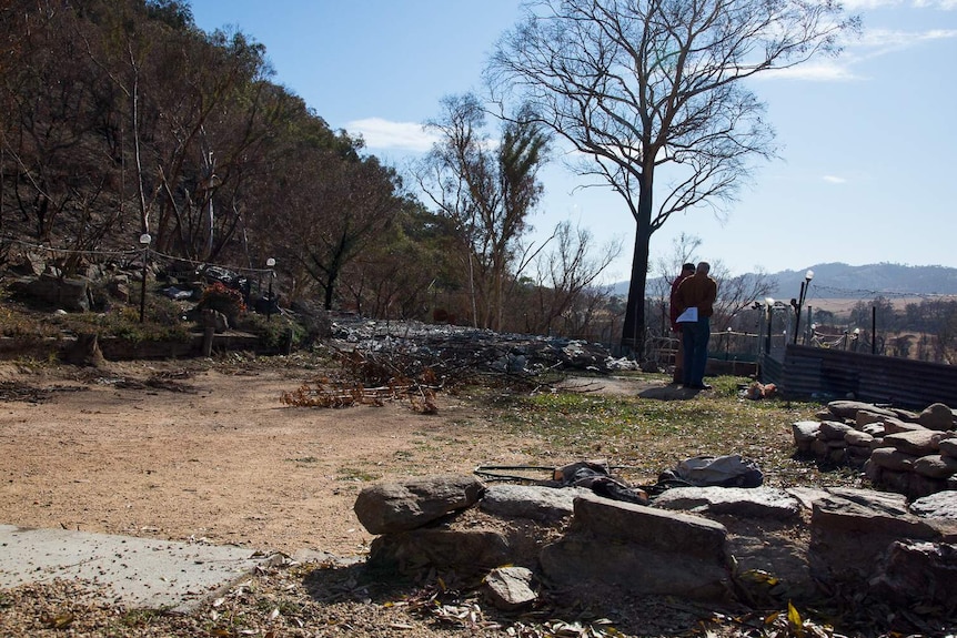 Two people look through burnt remains of a property.