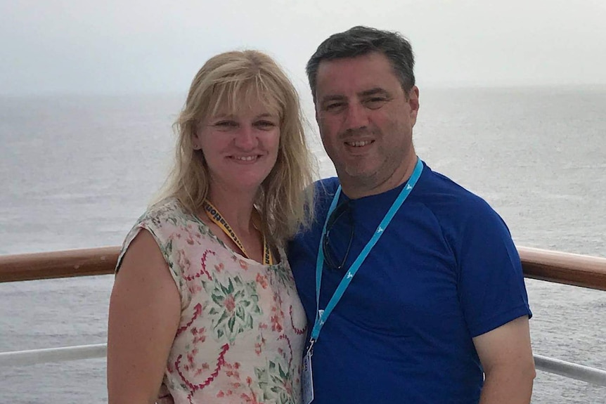 A couple stand together by a railing on a boat and smile