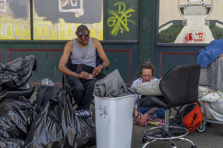 A homeless man and woman in Oregon. There are black rubbish bags in front of them.