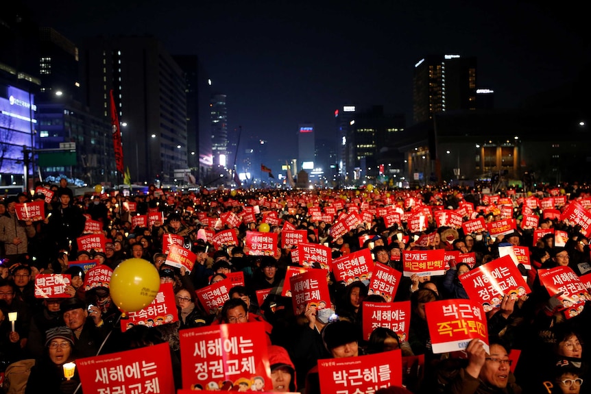 Large crowd of protesters waving signs through streets of Seoul. December 31, 2016.