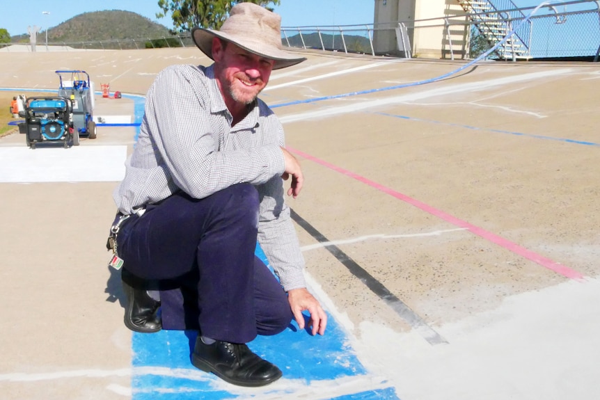 A man kneeling on a cycling track pointing at the concrete.
