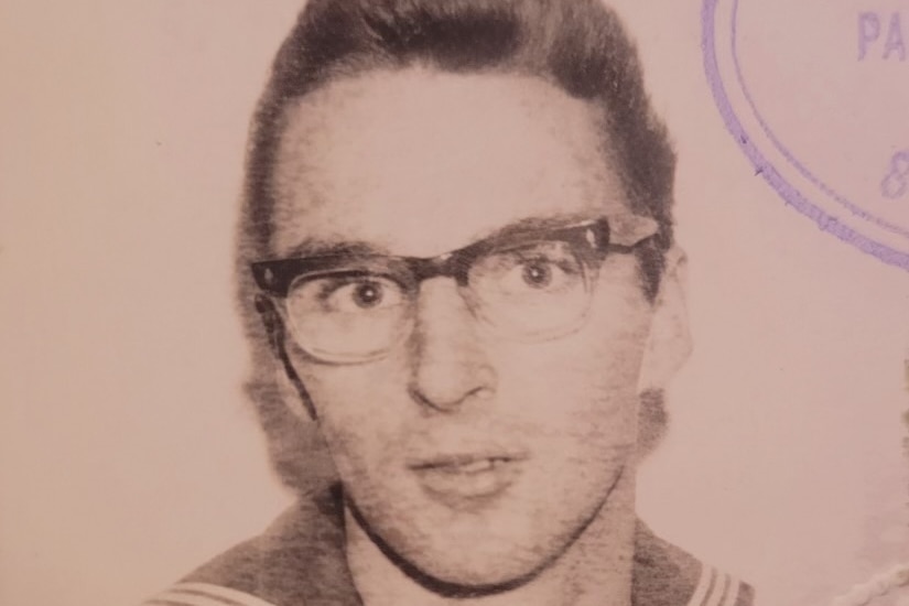 a vintage photo of a man in a sailor suit and thick-rimmed glasses posing for the camera