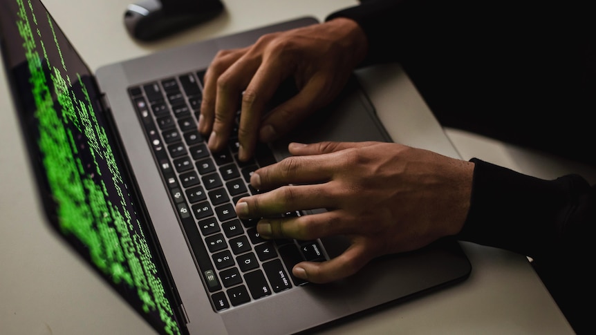 A computer with hacking software on the screen and someone's hands typing on the keyboard