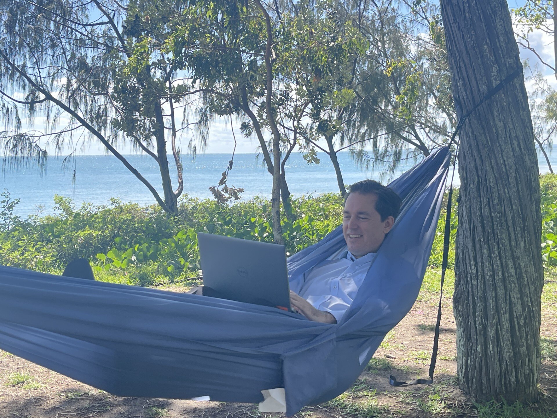 Man with brown hair holding a computer and lying in a hammock