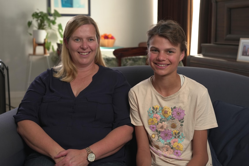 Mother and teenage daughter sitting on a sofa smiling.