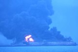 Smoke and flames are seen pouring from a tanker in the ocean.