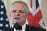 A close up of Scott Morrison with the US and Australian flags in the background.