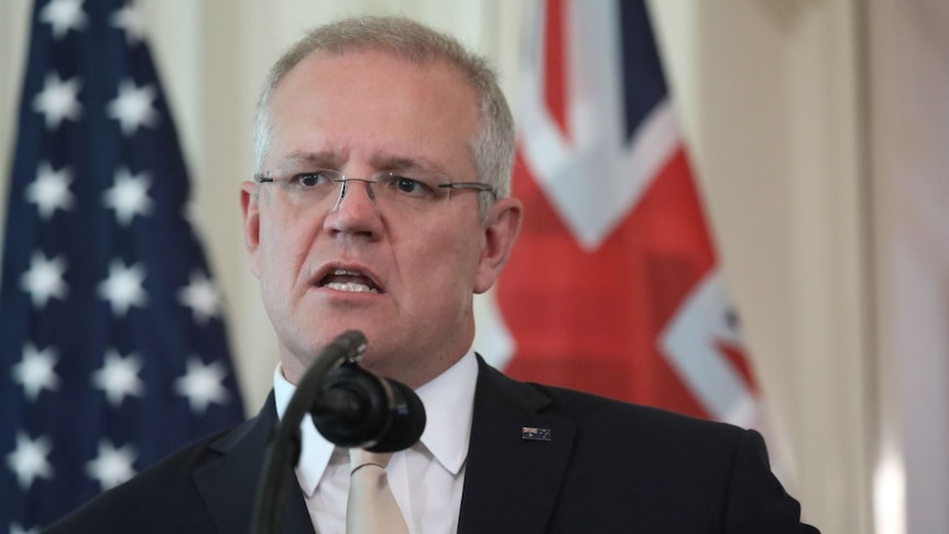 A close up of Scott Morrison with the US and Australian flags in the background.