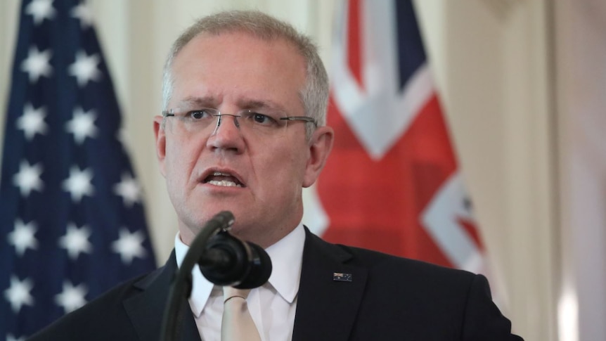 Scott Morrison speaks into a microphone with the Australian and US flags behind him.