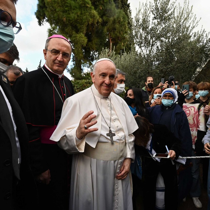 candid image of pope francis in white cassock gown with large cross necklace among crowd with facemasks on