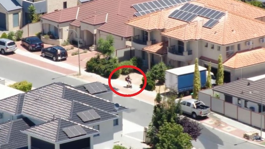 An aerial shot of a suburb with a person riding a scooter highlighted by a red ring
