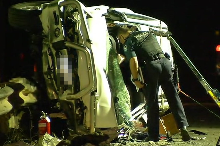 A police officer looks inside the wreckage of a four-wheel drive that is on its side against a guardrail after a head-on crash.