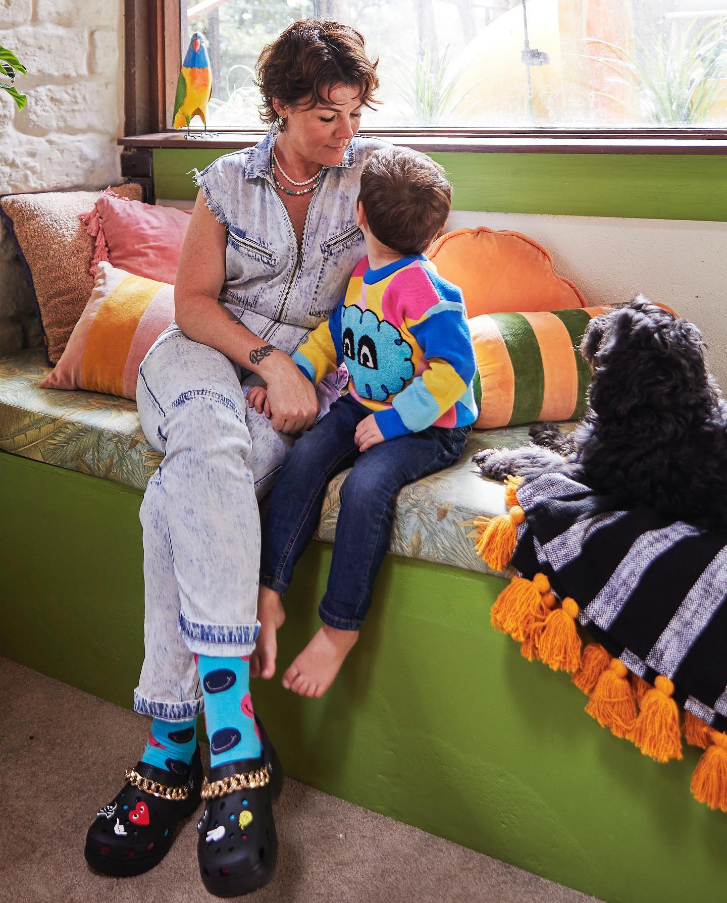 Em Rusciano viste un conjunto de mezclilla de dos piezas mientras se sienta en el sofá y mira a su joven sol.