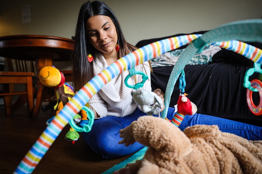 A woman looks down at her child lying under a colourful mobil