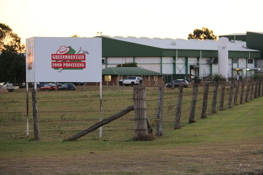 Greenmoutain Food Processing plant sign sits behind a barbed wire fence  in front of plant buildings.