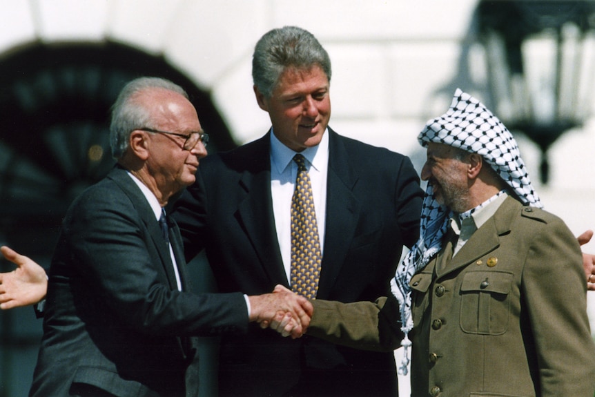 Two men shake hands as one man stands in between them.