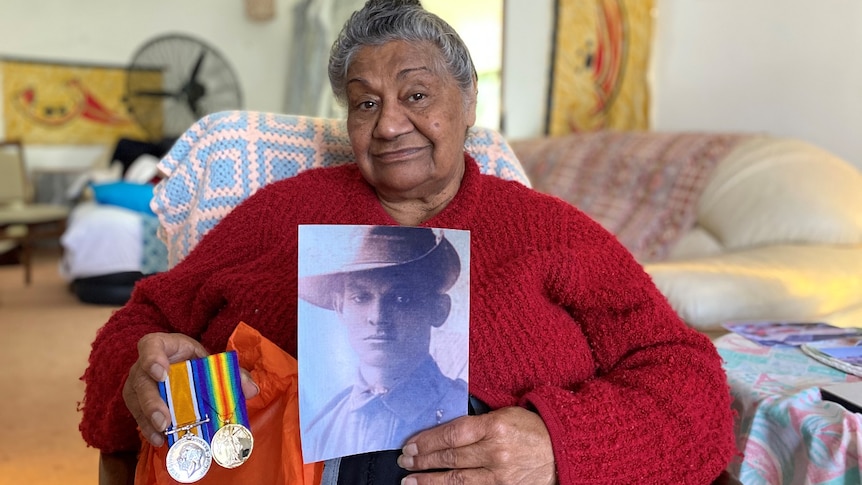 A woman holds a picture of a soldier and war medals