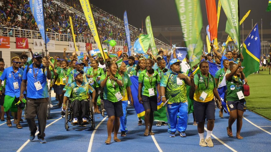 Athletes wearing blue and green march in the stadium.