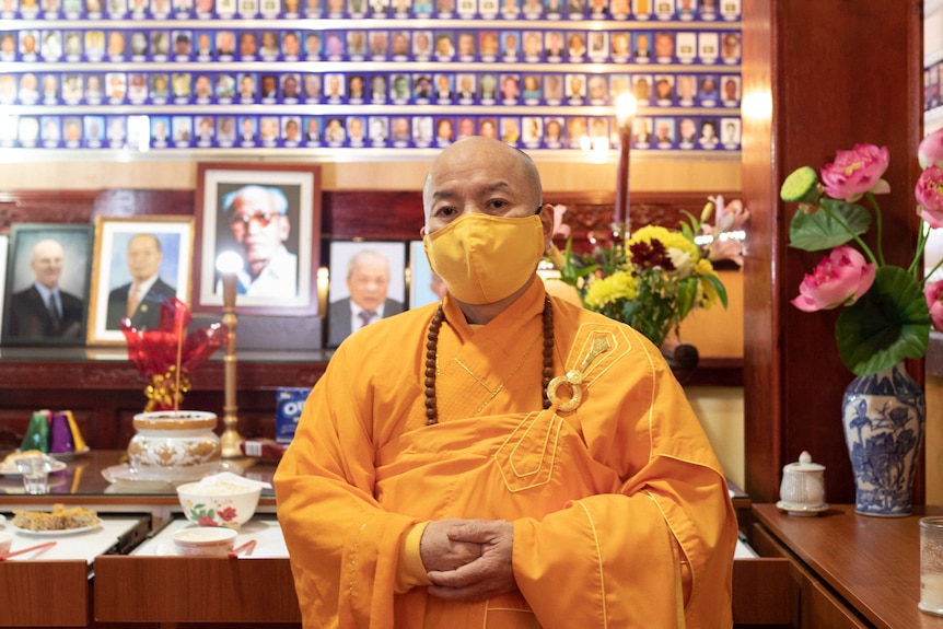 A man in a yellow robe standing in front of a memorial for the deceased.