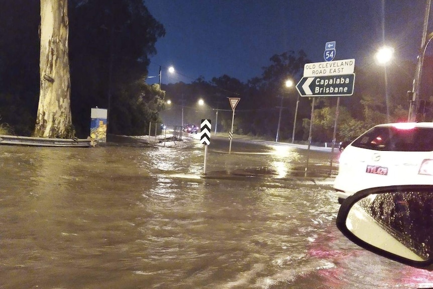 A flooded intersection with a road sign pointing to Brisbane and Capalaba.