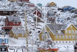 Fishing boats sit in the harbour of Uummannaq, with houses on a snow-covered slope behind.