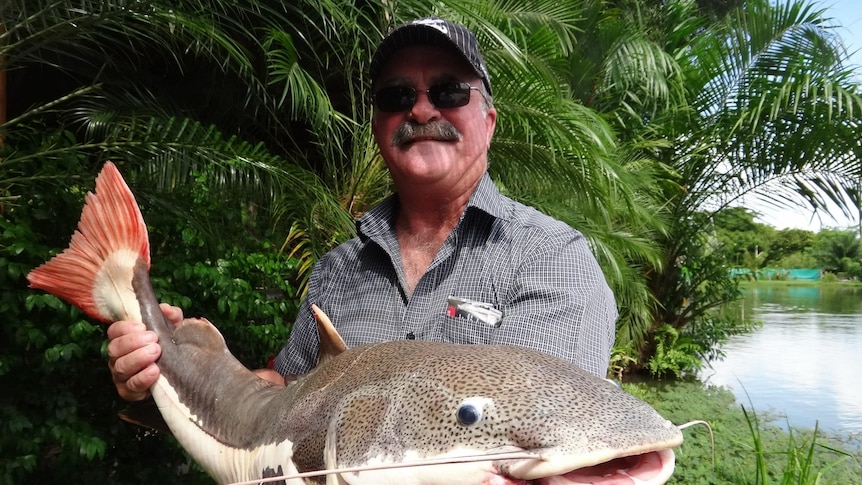 Man wearing sunnies and baseball cap holding a fish.