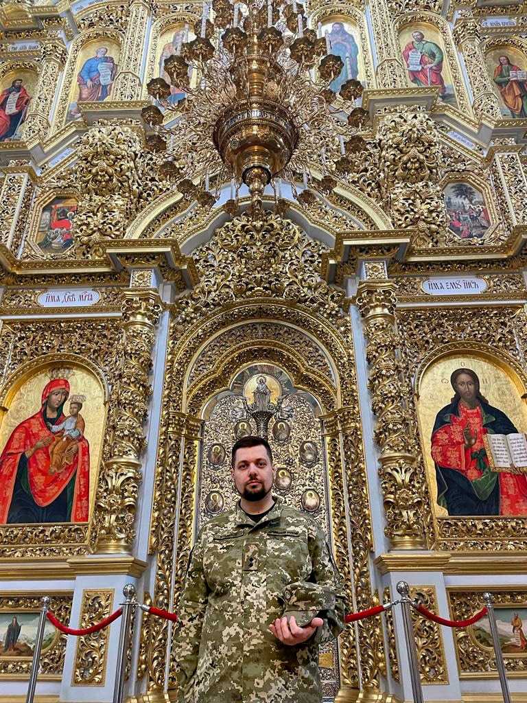 A man in army fatigues stands in front of an opulent gold altar 