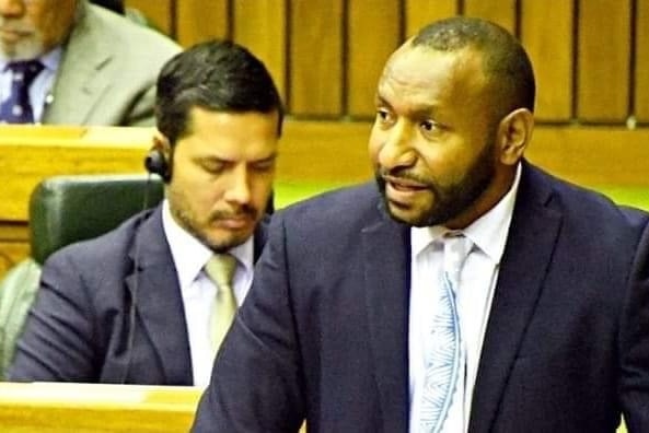 Rainbo Paita speaking in PNG parliament, wearing a suit.