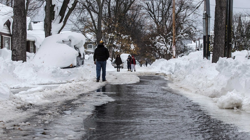 People walk down a street flowing with water in Buffalo.