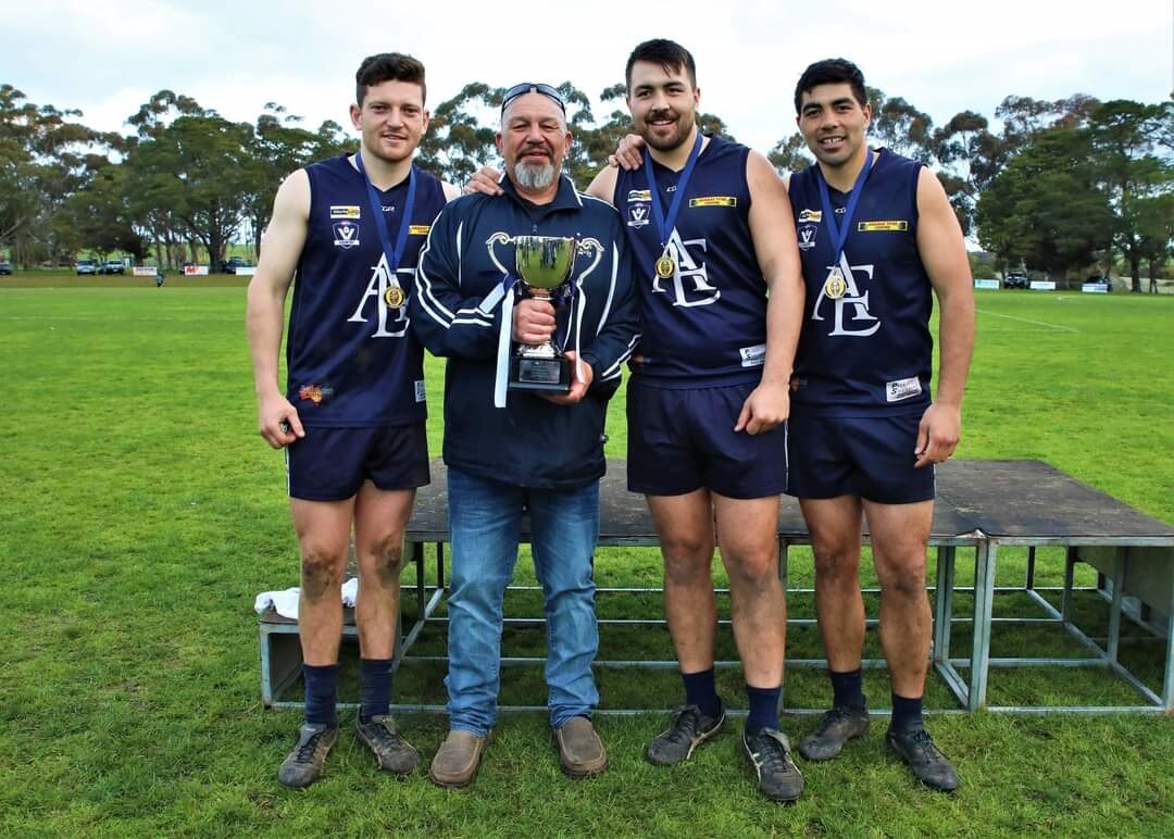 Four men stand next to each other, one holding a premiership cup 
